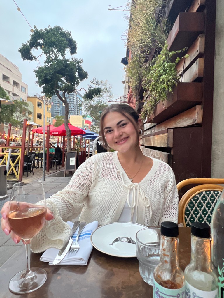 Marissa sitting at an outdoor restaurant, holding a glass of rosé wine