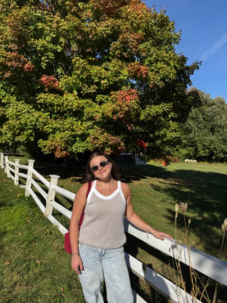 Marissa is leaning against a white fence.