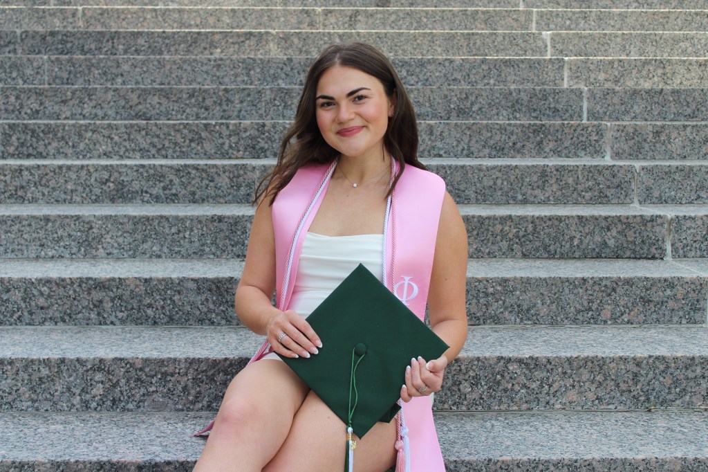 Marissa is sitting on steps holding a graduation cap.